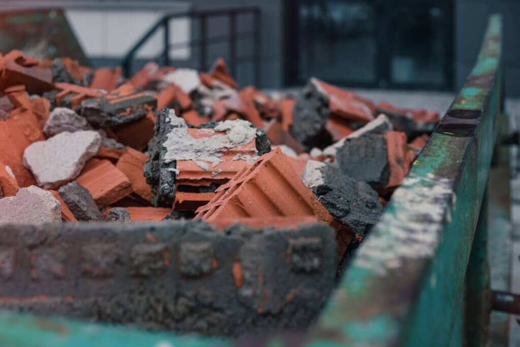 green metal skip with broken bricks